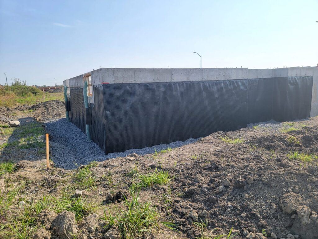 Dimpled drainage membrane wrapped around a new foundation, with gravel backfill